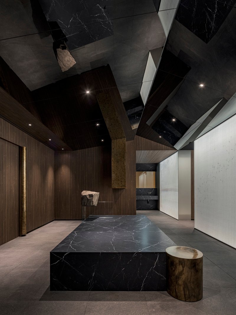 Entry area featuring the marble platform and cylindrical brass stool under geometric ceiling panels