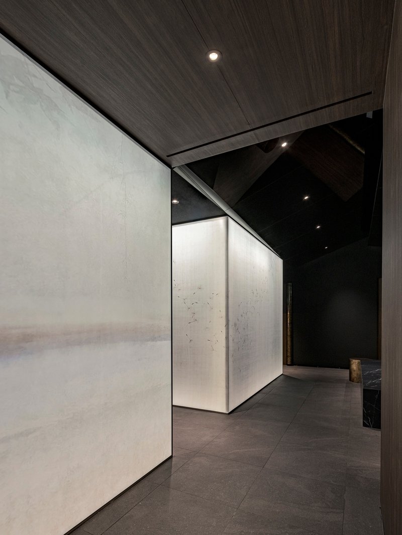 Corridor with pale stone wall panels and timber ceiling leading past a pivoting corner volume