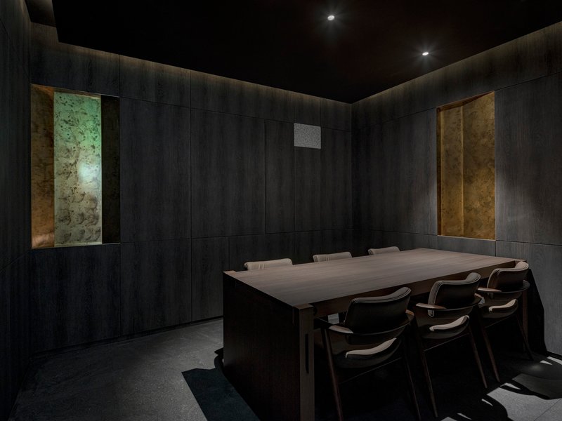 Private dining room with dark timber-paneled walls and backlit stone panels flanking the table