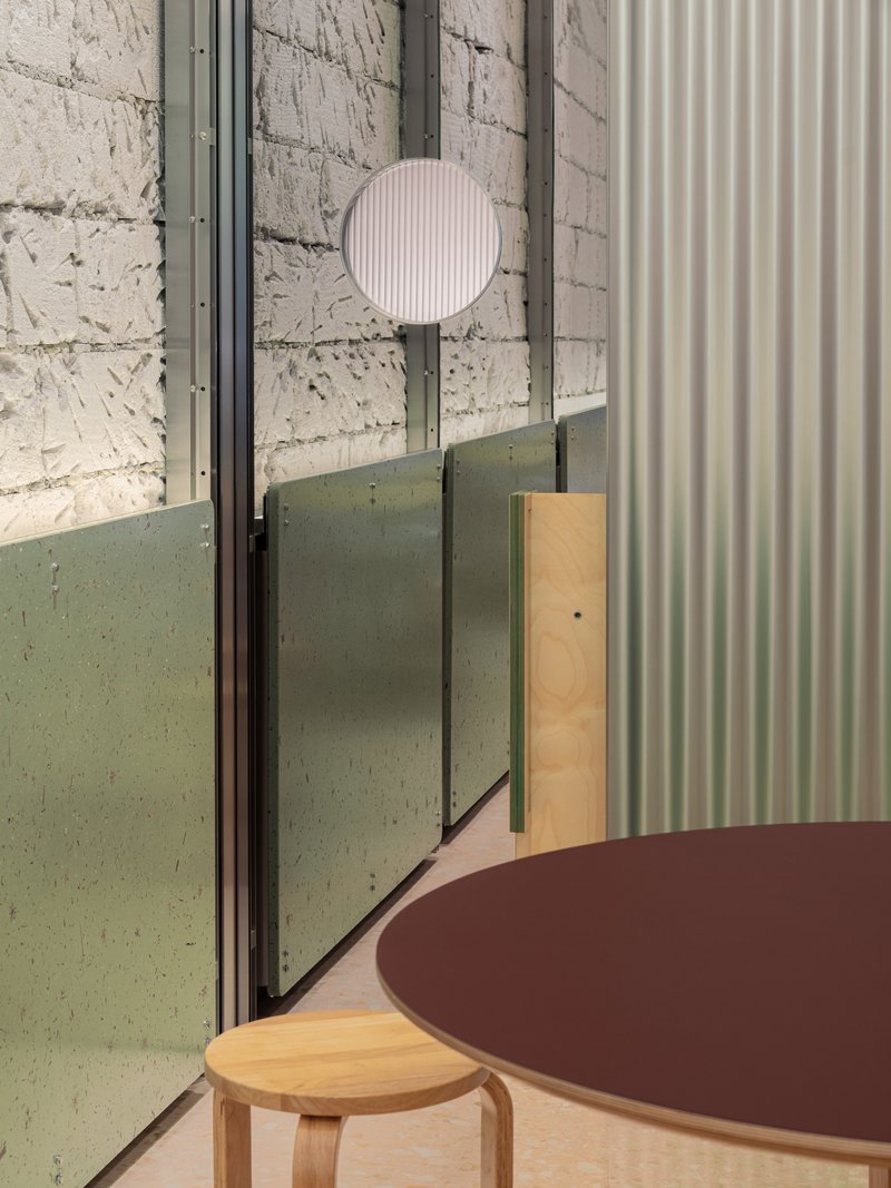 Interior detail of plywood table, pale green terrazzo panel and white fluted wall beside glass partition