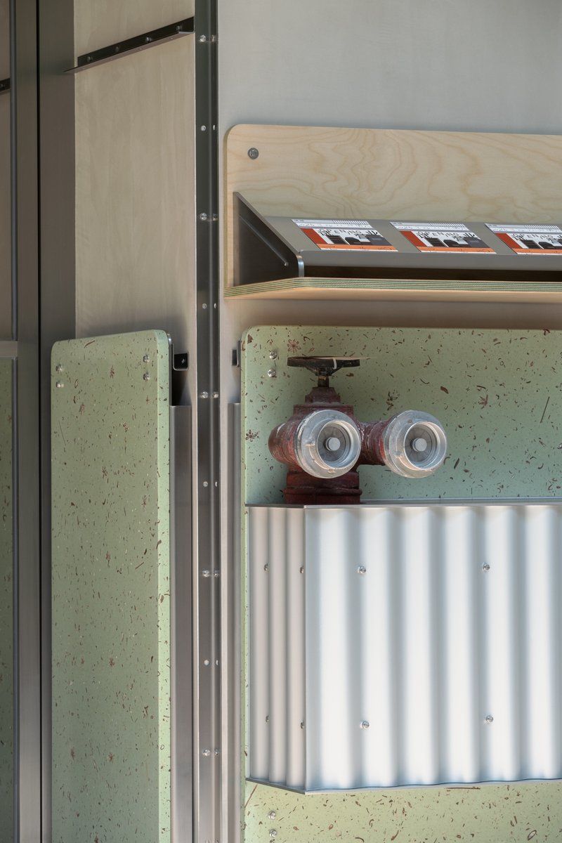 Close-up of exposed water valve and pipes mounted on pale green terrazzo wall beneath plywood shelf