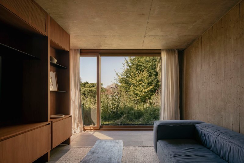 Sitting room with timber millwork and board-formed concrete walls framing a garden view