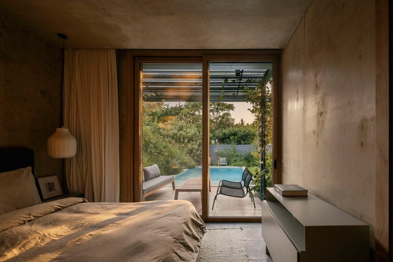 Bedroom with timber-framed glazing overlooking the pool terrace at dusk