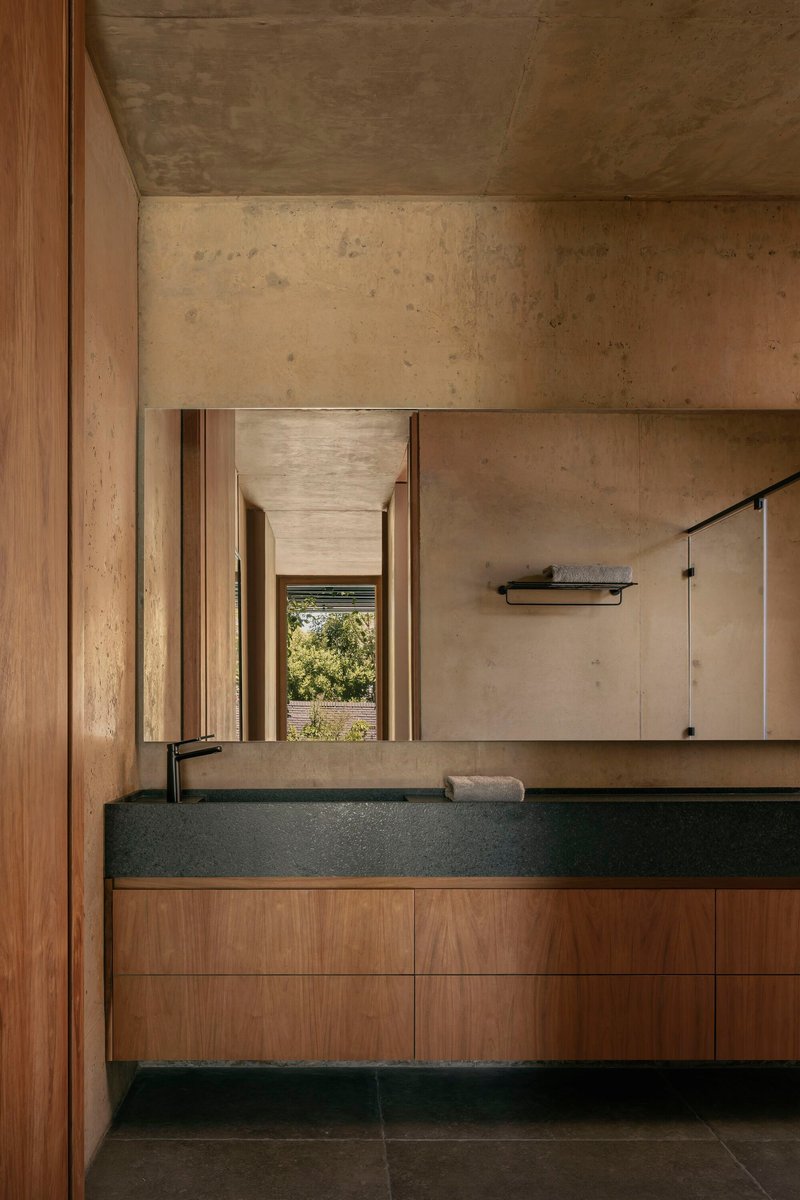 Bathroom vanity with black stone countertop and timber cabinetry beneath exposed concrete ceiling