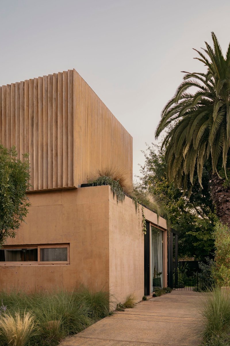 Stucco facade with vertical timber screen above and garden pathway flanked by palm trees