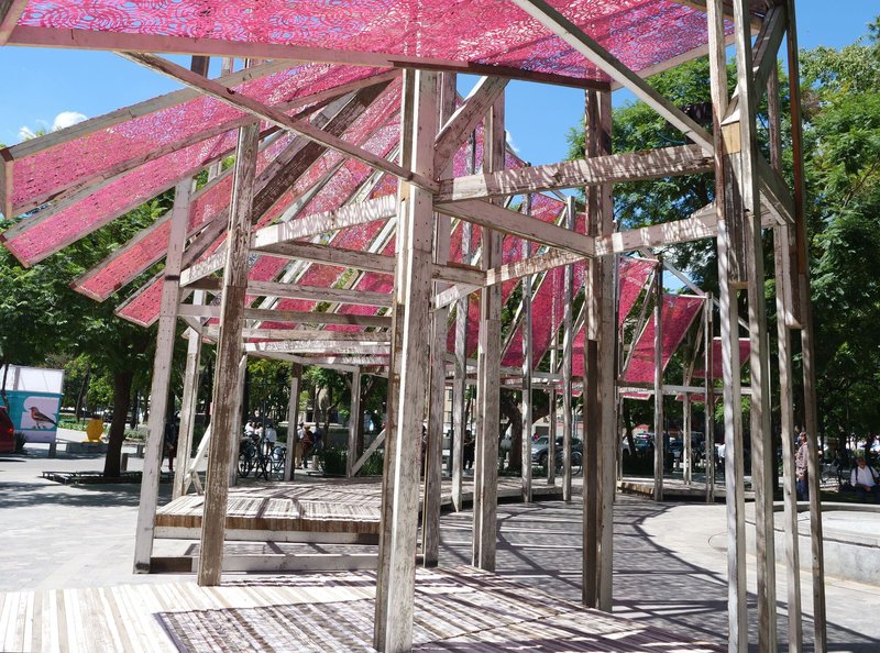 Interior view beneath the angled timber frame structure showing cross bracing and translucent pink canopy overhead
