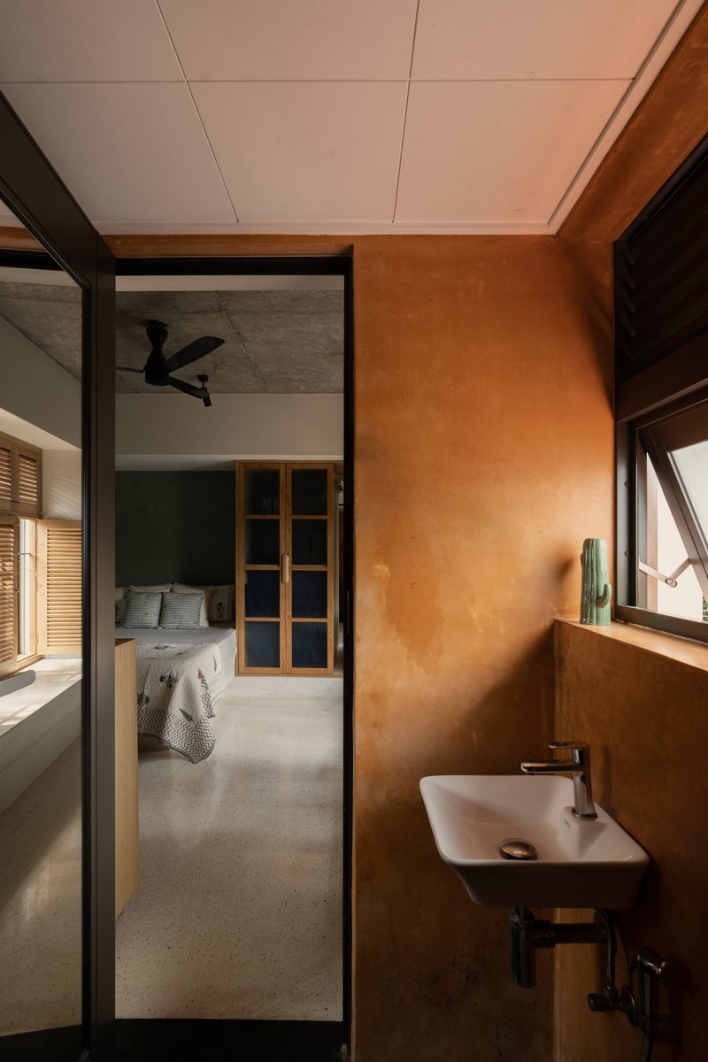 Bathroom with terracotta plaster walls and view through glazed door to bedroom with ceiling fan