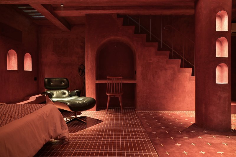 Red plaster interior with arched niches, metal staircase, and cross-pattern tile floor beneath timber ceiling beams