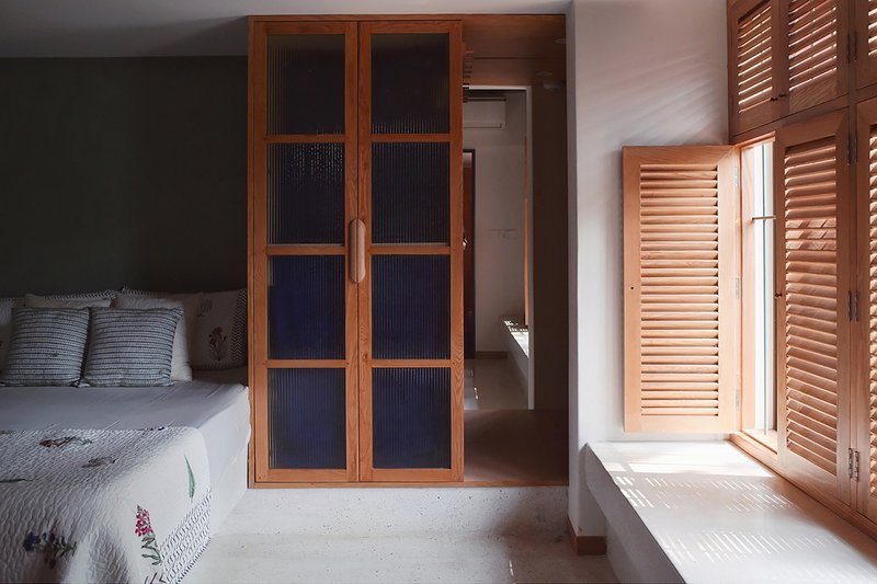 Bedroom with timber-framed glass doors and louvered shutters filtering daylight onto pale concrete floor