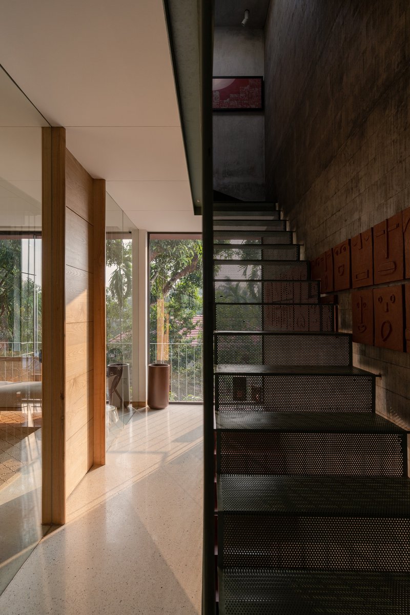 Perforated metal staircase rising beside timber storage wall and glazed doors with garden beyond