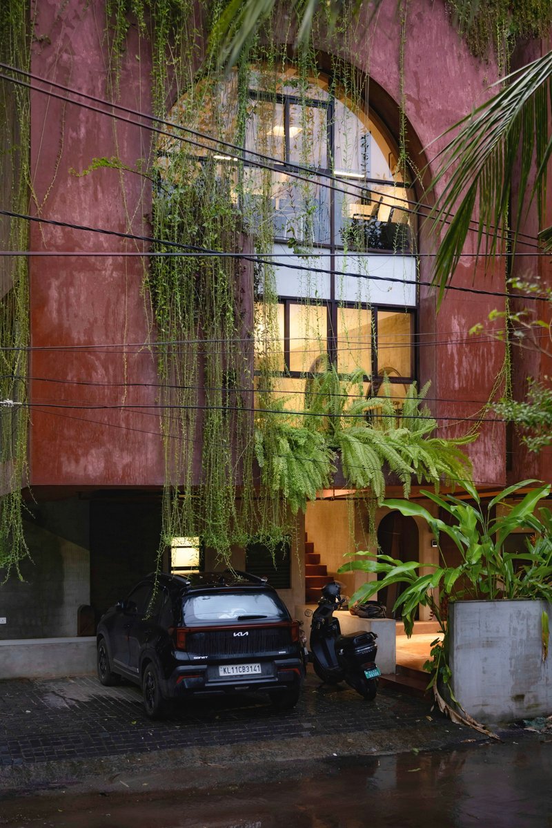 Pink rendered facade with arched glazed opening and cascading greenery above a wet driveway at dusk