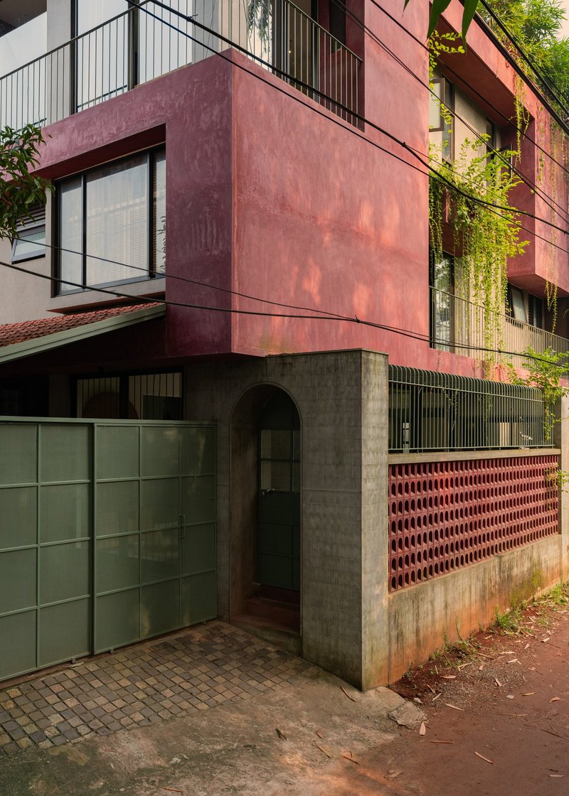 Corner entry with concrete portal and terracotta perforated screen wall beneath cantilevered red oxide volume