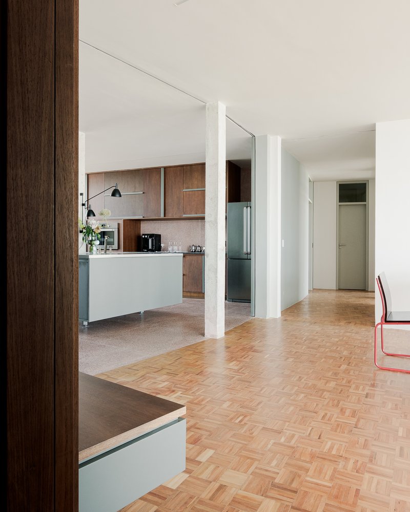 Open living space with herringbone parquet flooring transitioning to terrazzo in the kitchen area