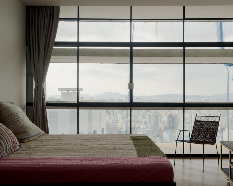 Floor-to-ceiling glazing framing a hazy cityscape with dark curtains and woven lounge chair