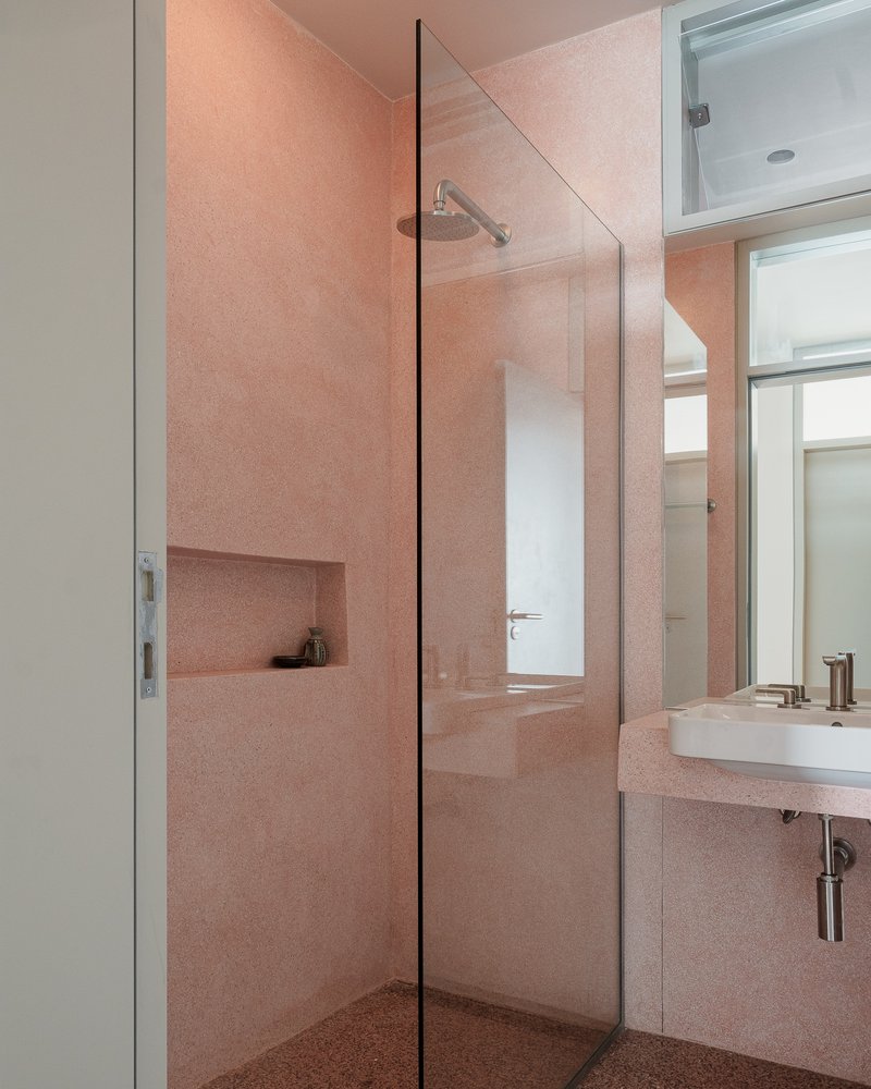 Pink terrazzo bathroom with glass shower partition and recessed wall niche under soft ceiling light