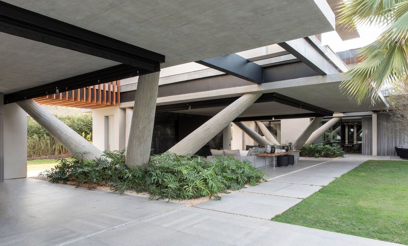 Underside of concrete slab supported by diagonal columns sheltering a planted garden and lawn