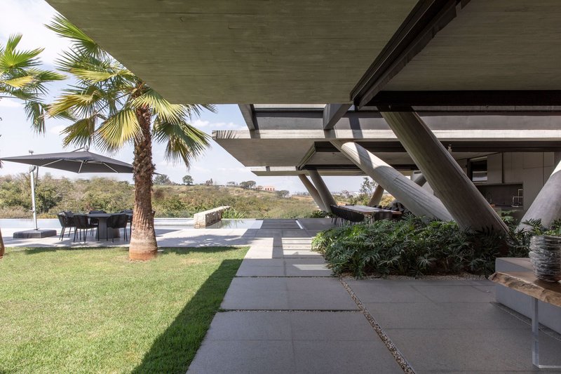 Large concrete pavers crossing the lawn beneath angled structural supports and palm trees