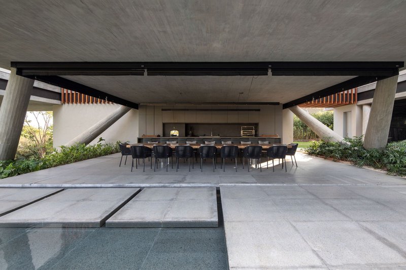 Outdoor dining area under concrete soffit with angled columns flanking the long table and pool edge