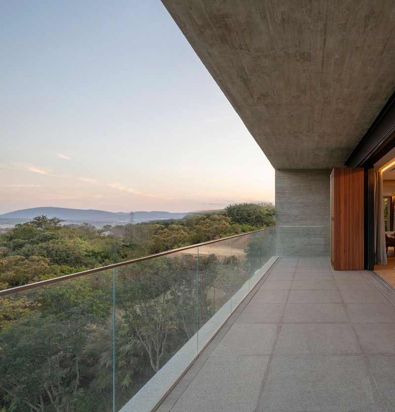 Concrete terrace with glass balustrade overlooking a forested valley at dusk
