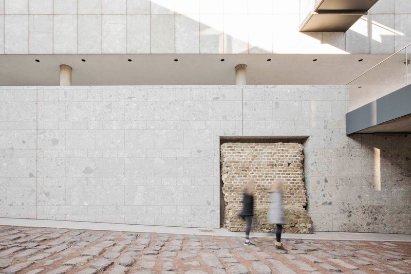 Recessed window opening in pale stone wall revealing historic brickwork with two figures walking past