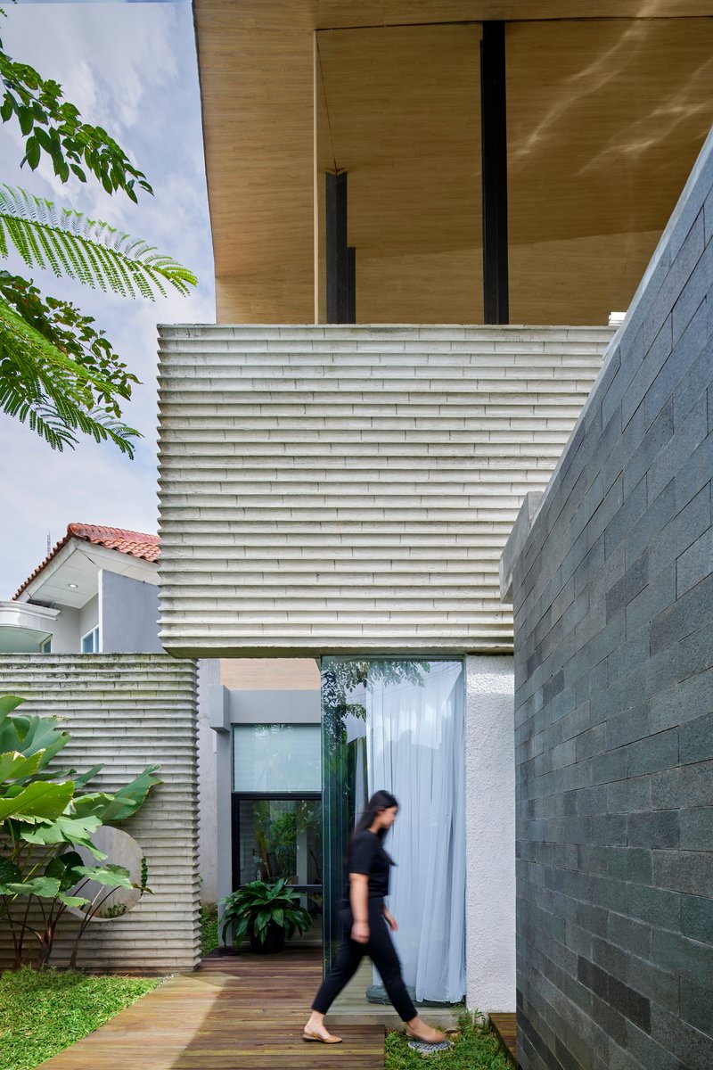 Timber deck walkway beneath cantilevered plywood soffit with horizontal louvered screen and person in motion