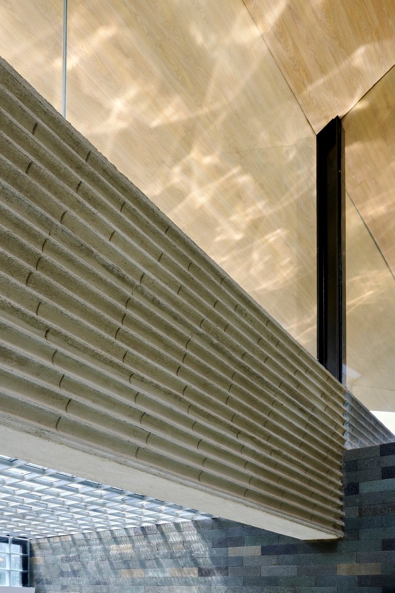 Close-up of horizontal concrete louvered screen meeting plywood soffit with dappled shadows falling across surfaces
