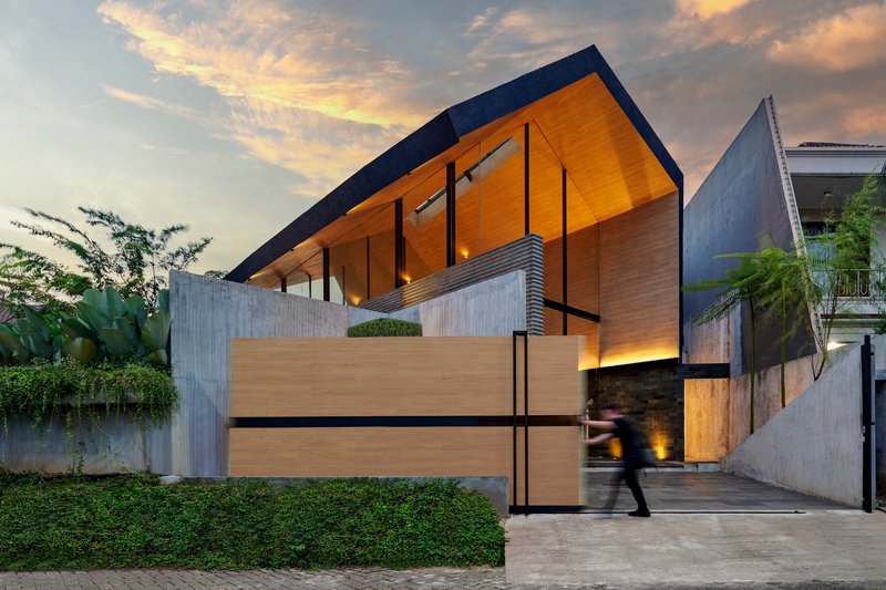 Street view of the timber-clad entrance with pivoting gate and figure walking into the courtyard at dusk