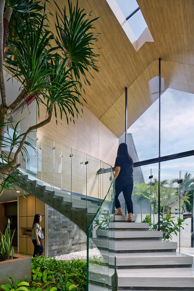 Interior staircase with glass balustrade rising through the double-height space with palms and skylight above