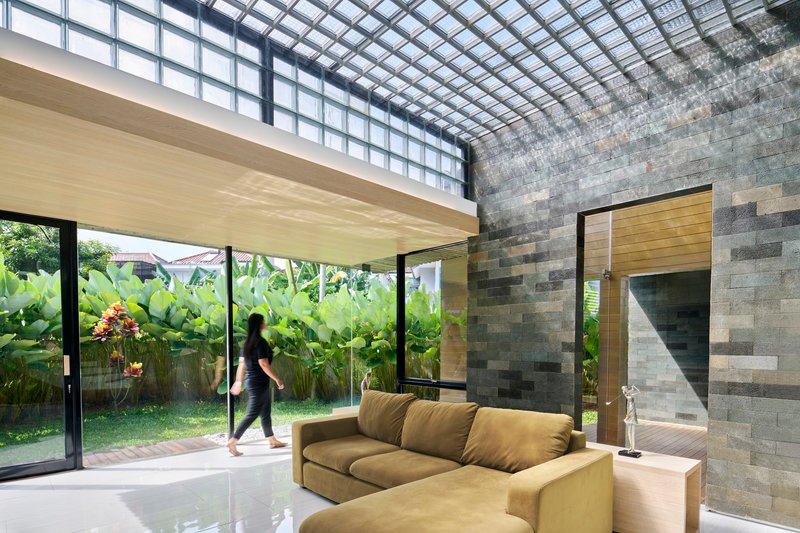Living space beneath a gridded skylight opening to a garden with banana plants beyond glass doors