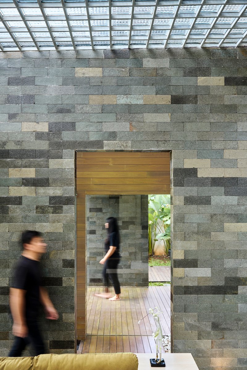 Timber-framed doorway through a variegated stone block wall with people passing beneath a slatted skylight