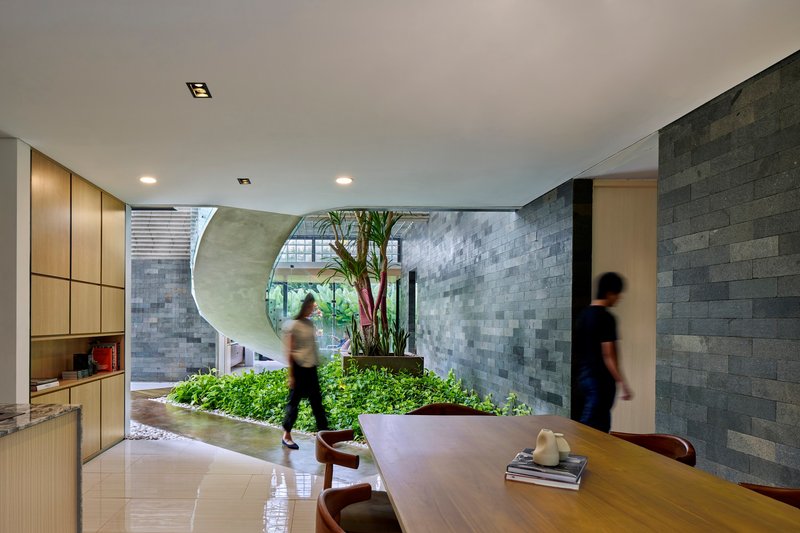 Open-plan living space with circular void to courtyard garden and people moving through planted interior beds