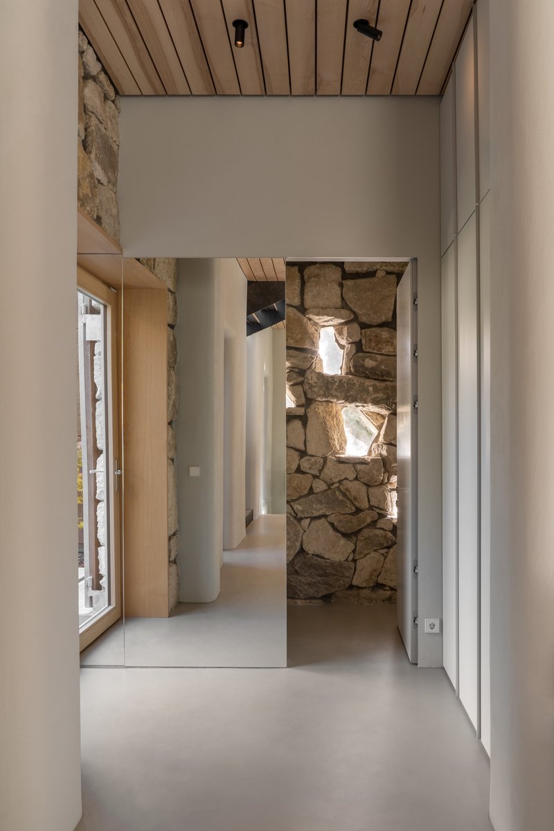 Interior hallway with slatted timber ceiling and exposed stone wall illuminated by natural light