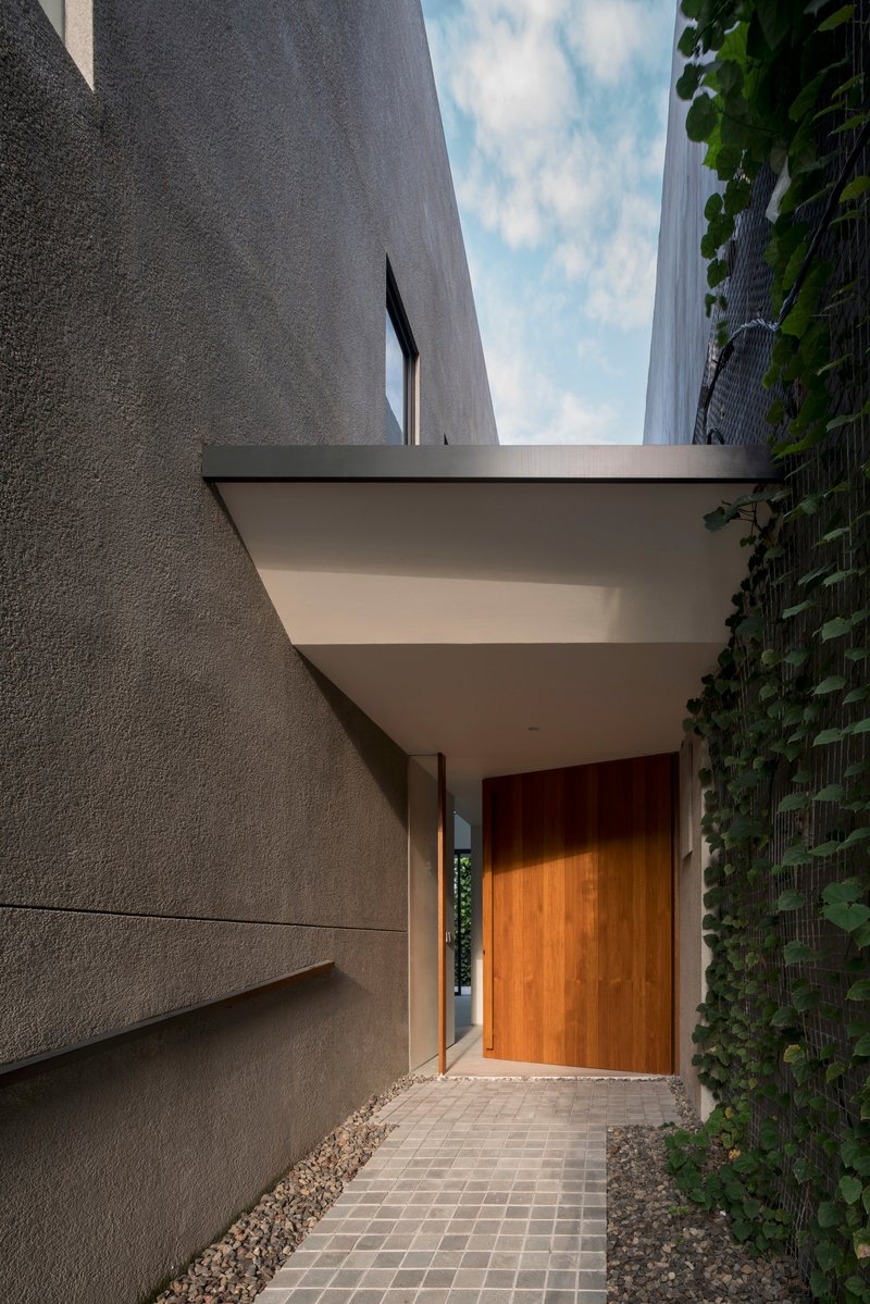 Entry path with wood door and canopy between textured concrete walls and a green wall at dusk