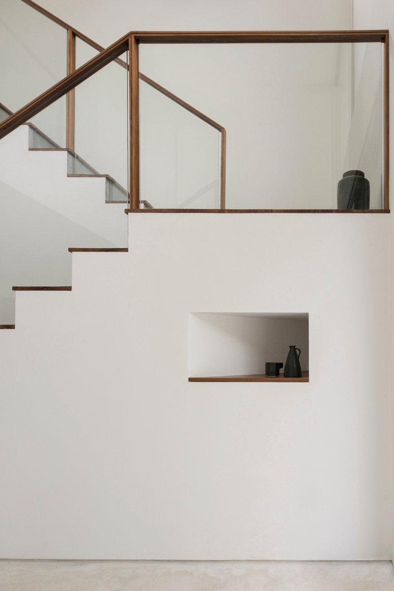 White staircase with timber-framed glass balustrade and recessed display niche holding ceramic vessels