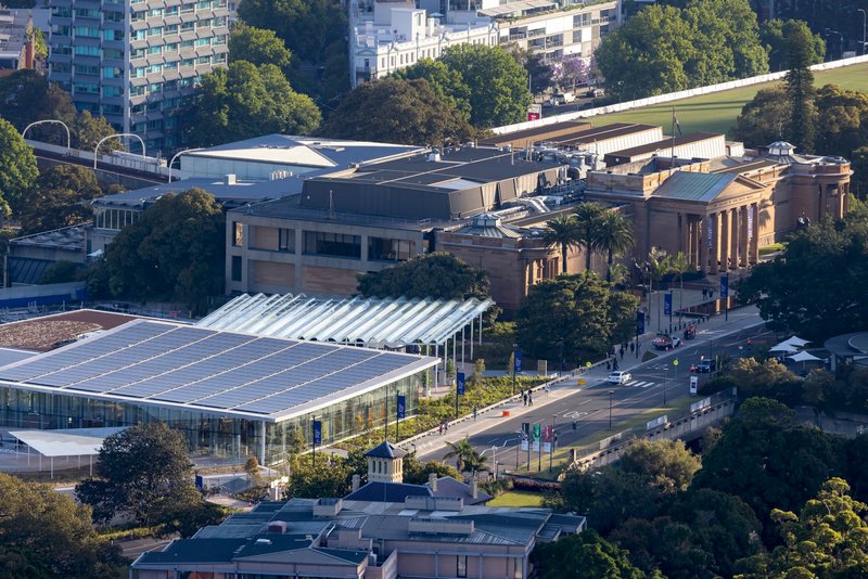 Aerial view showing the angular metal roof volumes nestled among trees and adjacent to a columned classical building