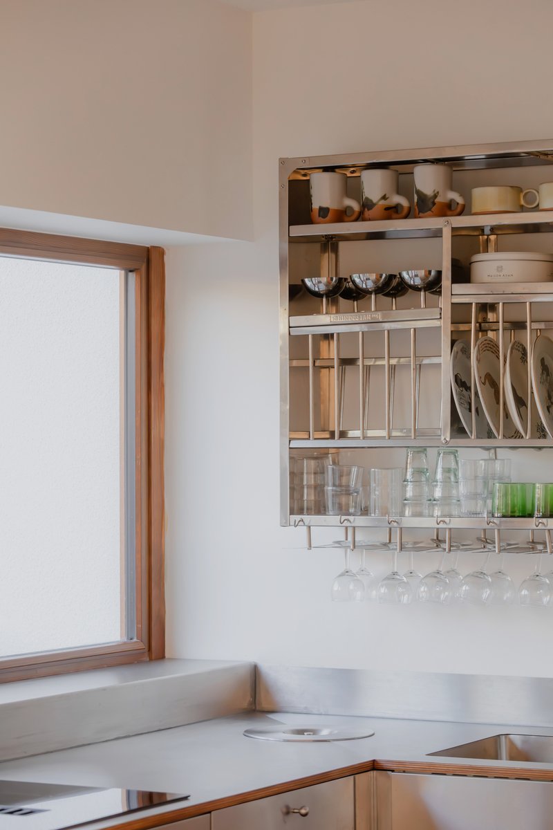 Open kitchen shelving with compartments for cookware, utensils, and glassware beside timber-framed window