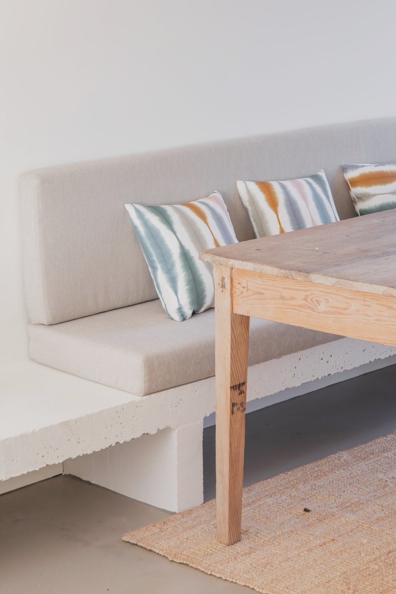 Built-in concrete bench with upholstered cushions and striped pillows beside timber table