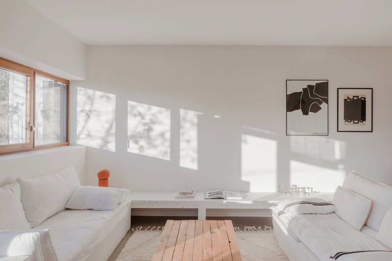 White interior living room with timber-framed windows casting sharp rectangular shadows across the floor