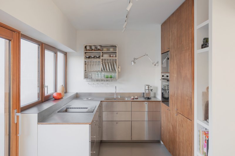 Compact kitchen with stainless steel countertops and timber cabinetry beside a row of timber windows