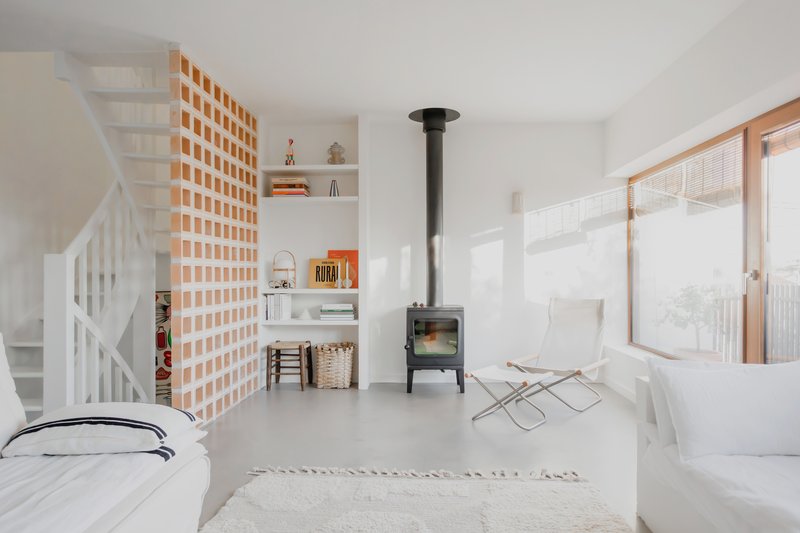Open-plan interior with timber lattice screen, black wood stove and white staircase under afternoon sunlight