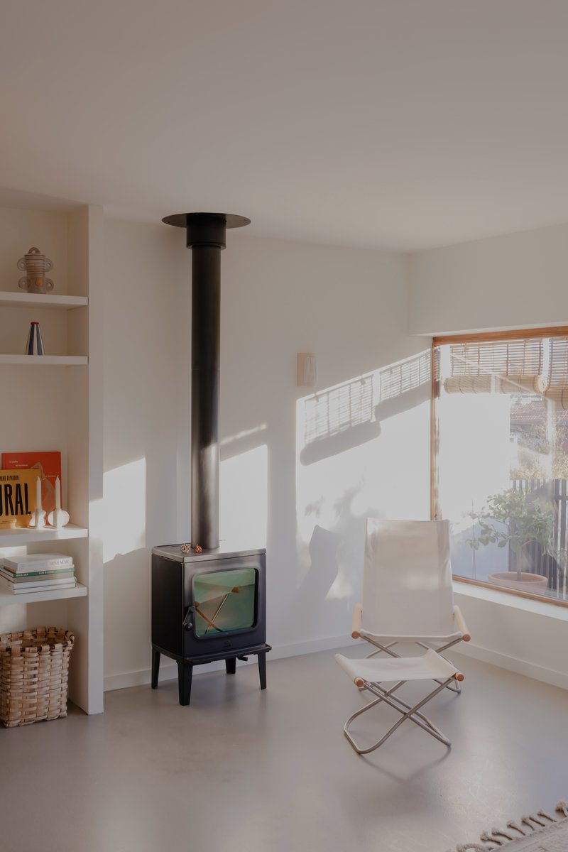 Black freestanding wood stove beside canvas lounge chair with afternoon sun casting window shadows on white walls