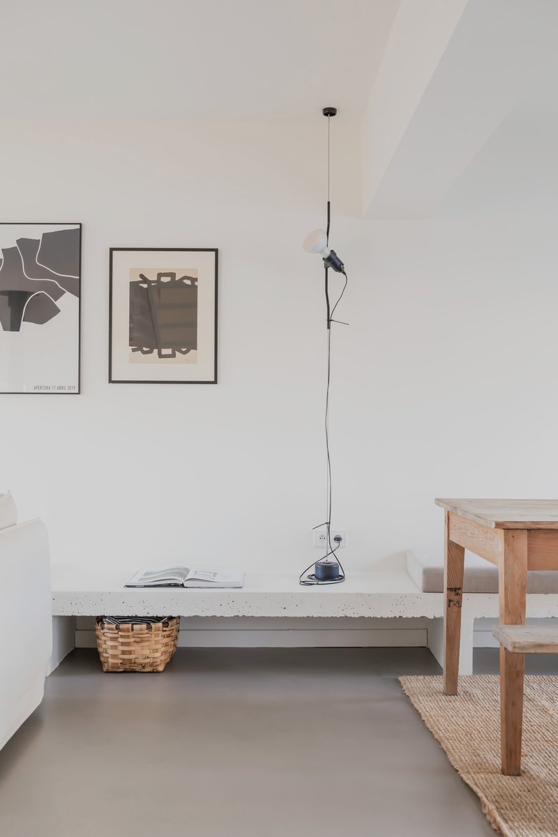 White living room with concrete bench, pendant lamp, framed artworks and grey polished floor