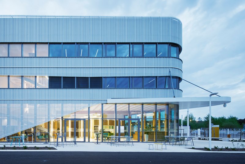 Ground floor terrace with outdoor seating beneath the curved glass facade at twilight