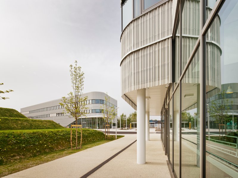 Curved translucent facade with white columns set against a grass berm and young trees
