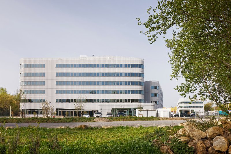 Horizontal striped facade of six-story office building viewed across wild grasses and boulders