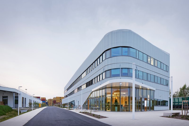 Curved corner entry facade with floor-to-ceiling glass and ribbed metal cladding at dusk