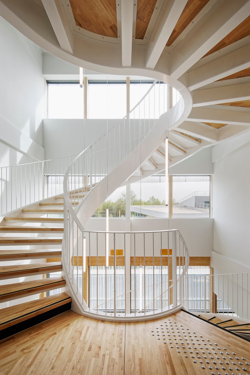 Spiral staircase with white metal railings and timber treads rising through a multi-story atrium