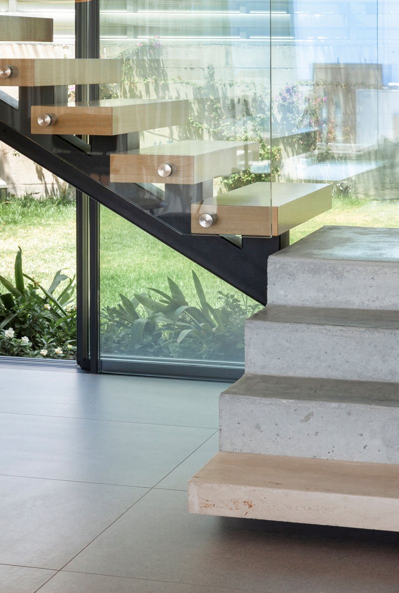 Concrete treads with timber nosings and black steel stringer beside floor-to-ceiling glass wall with garden beyond