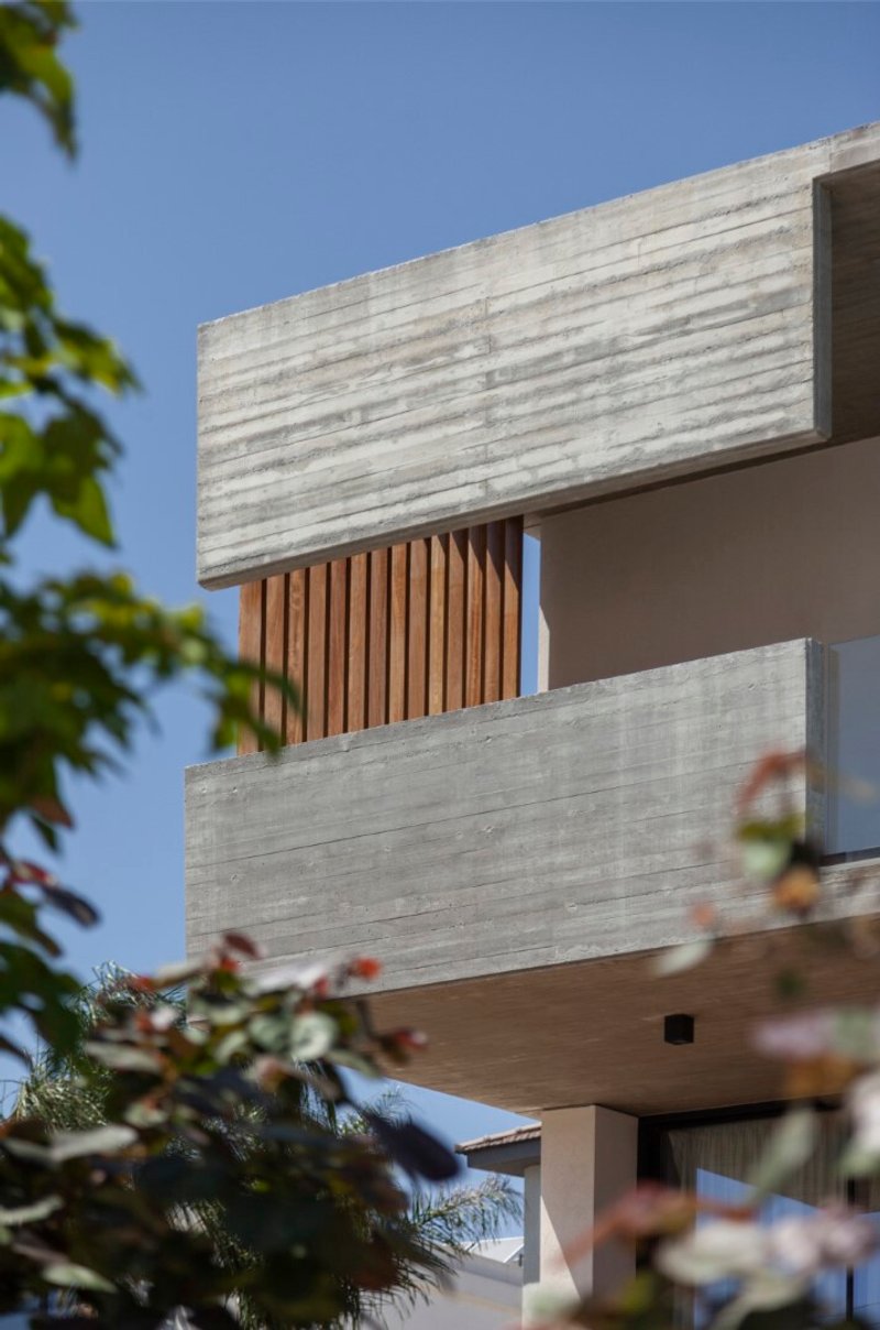 Stacked concrete volumes with vertical timber screening seen through foliage against a clear blue sky