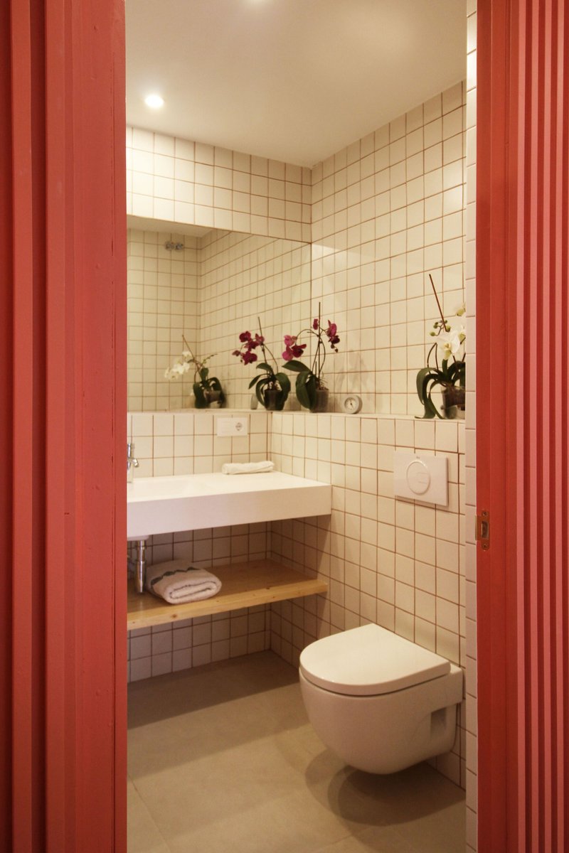 View through red corrugated panel doorway to bathroom with cream square tile walls and orchids on shelf